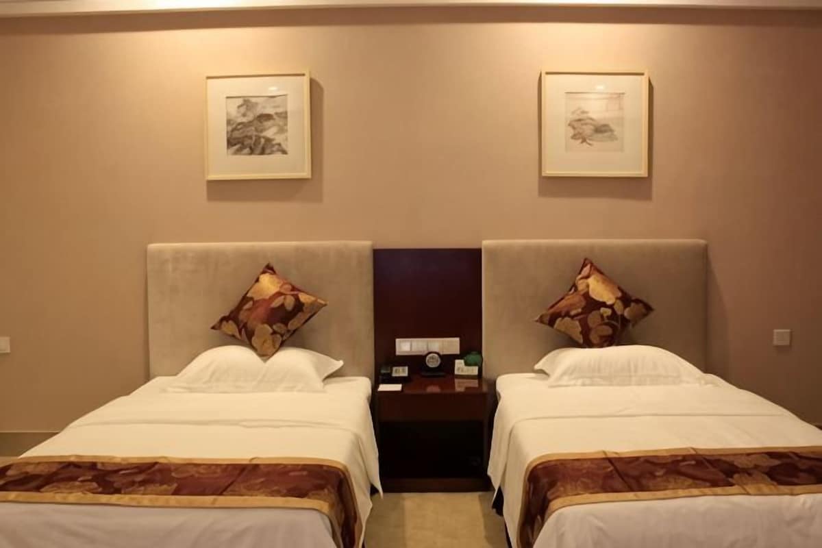 A hotel room with two beds, each with a headboard, a nightstand, a clock, and a framed picture on the wall.