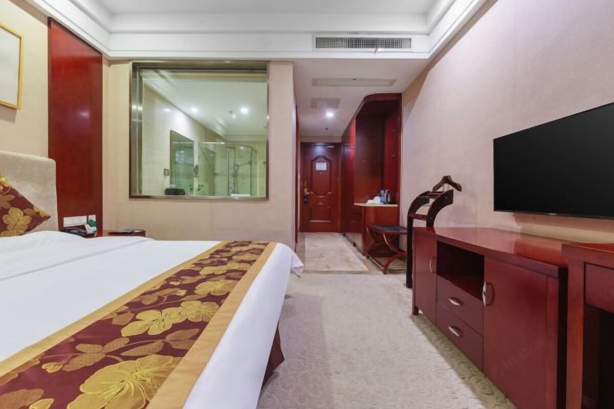 Une chambre d’hôtel avec un grand lit, un bureau, une chaise, une télévision et un miroir.