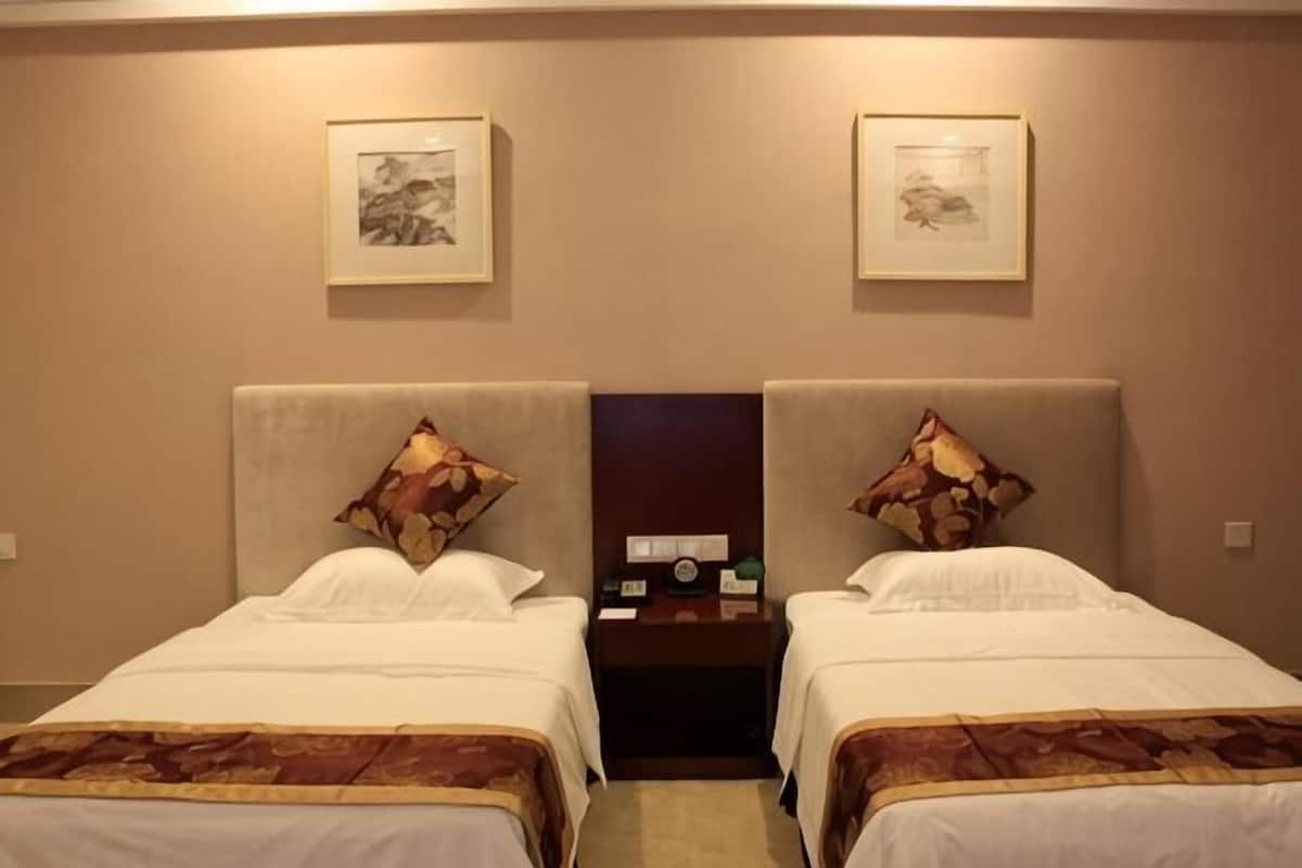 A hotel room with two beds, each with a headboard, a nightstand, a clock, and a framed picture on the wall.