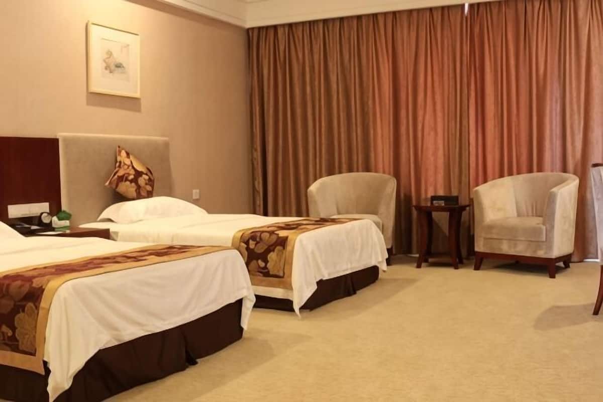 A hotel room with two beds, a chair, a small table, and a large window with curtains.