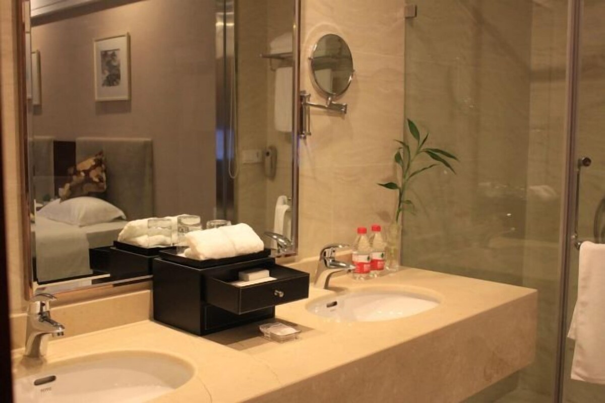 Une salle de bain d’hôtel avec deux lavabos, un miroir, une douche en verre et une table de chevet avec une serviette.