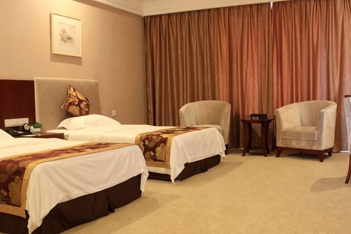A hotel room with two beds, a chair, a small table, and a large window with curtains.