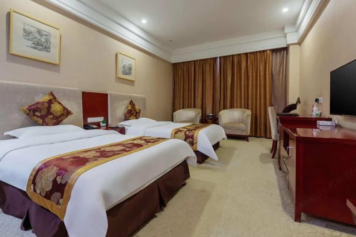Une chambre d’hôtel avec deux lits, un bureau, une chaise et un téléviseur.