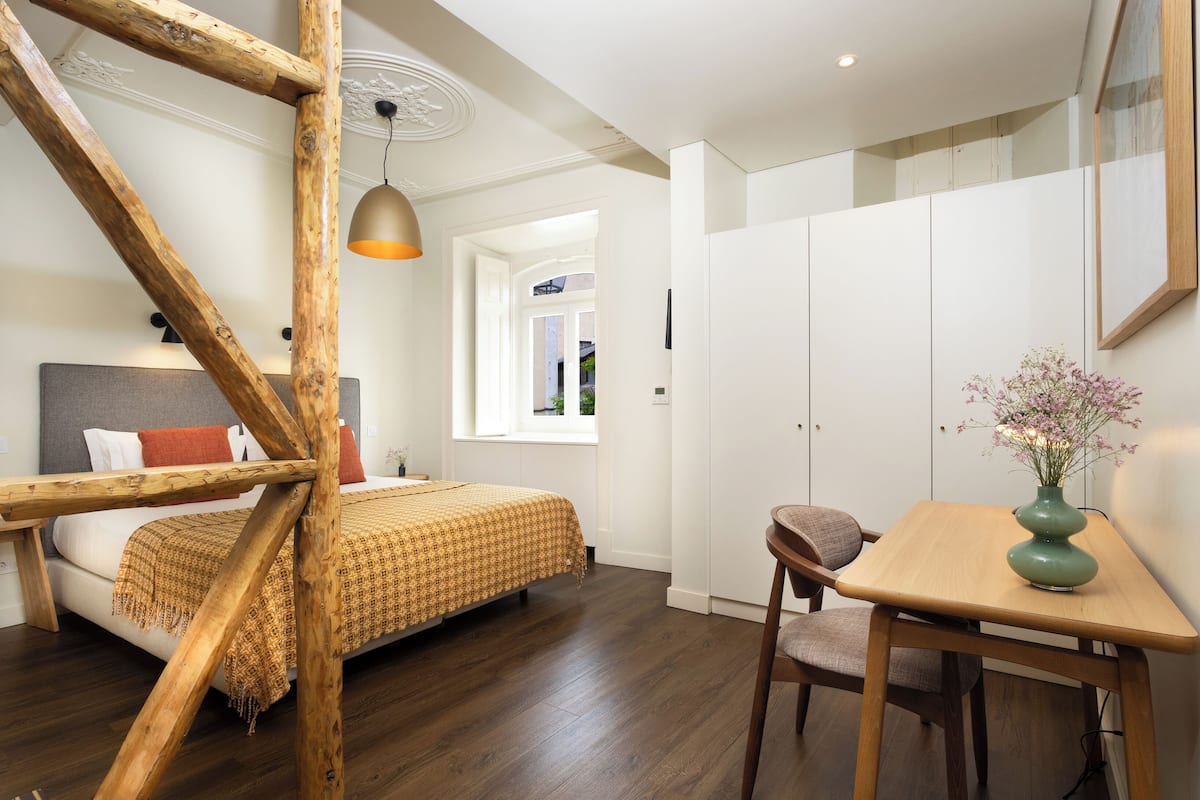 Une chambre à coucher avec un lit, une échelle en bois, une table, une chaise et un vase rempli de fleurs.