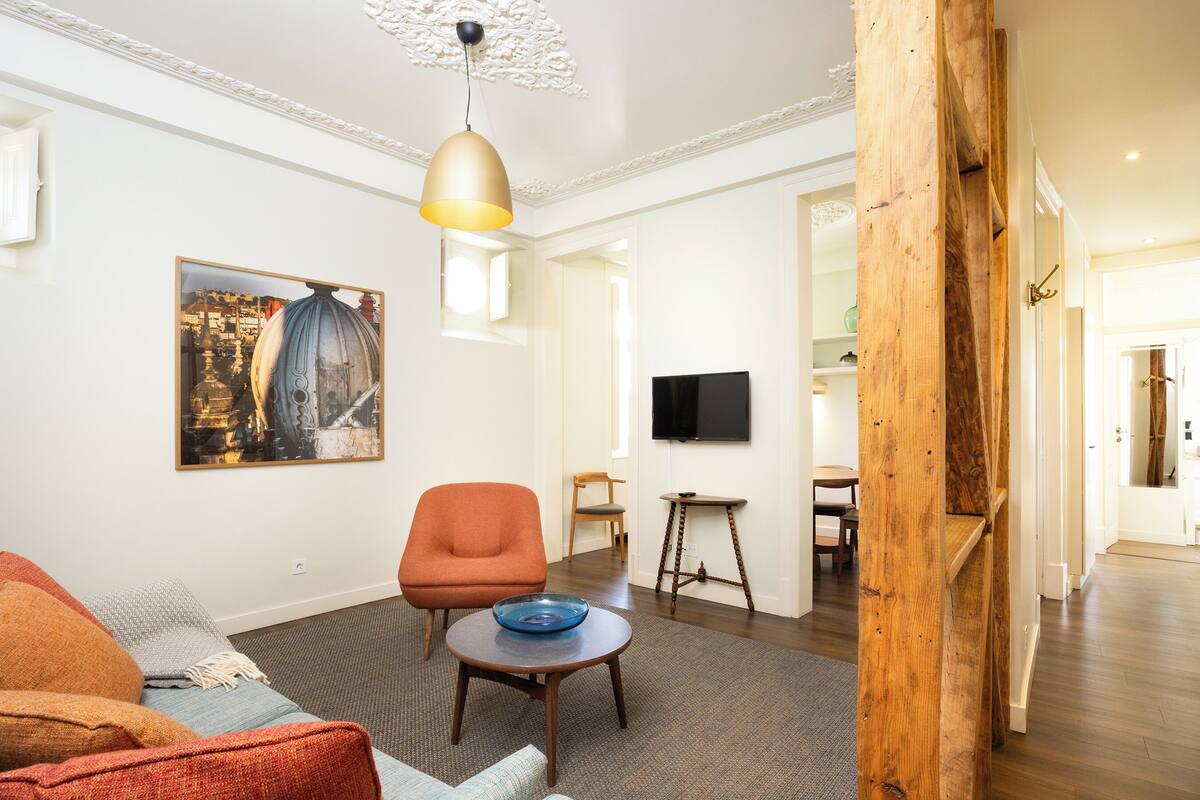 Un salon avec un canapé, un fauteuil, une table sur laquelle se trouve un saladier, un tableau et un téléviseur.