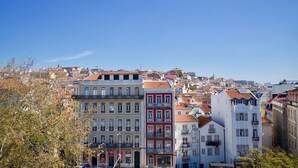 Eine Stadtansicht mit verschiedenen Gebäuden, darunter ein markantes weißes Gebäude mit Balkonen und ein rotes Gebäude ebenfalls mit einem Balkon.