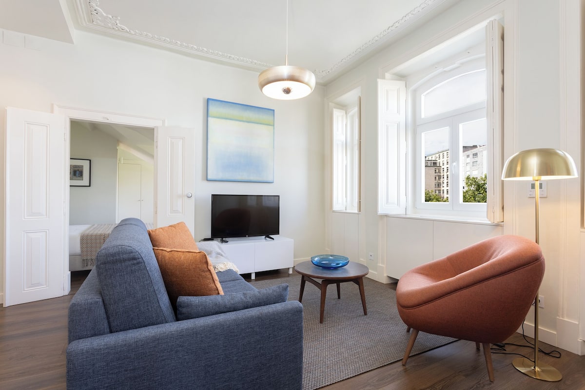 Un salon moderne avec un canapé, un fauteuil, un téléviseur et des œuvres d’art accrochées au mur.