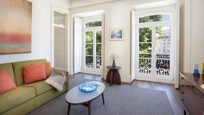 Ein Wohnzimmer mit einem grünen Sofa, einem Couchtisch mit einer blauen Schale, einem Bild an der Wand und Blick durch Glastüren.