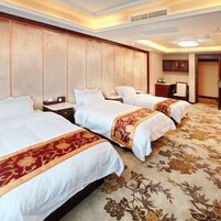 Habitación de hotel con tres camas, cabecera de madera, alfombra floral y una mesita de noche con lámpara.