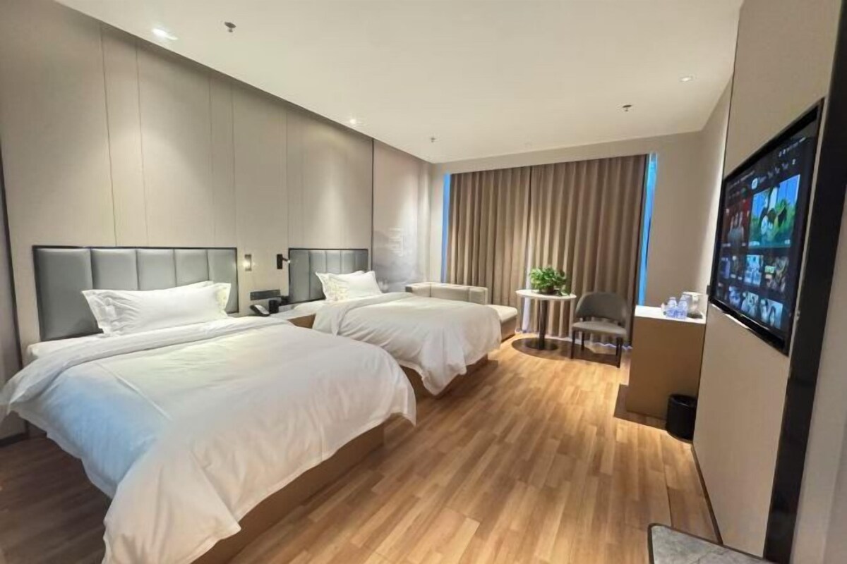 A hotel room with two beds, a desk, a chair, and a television.