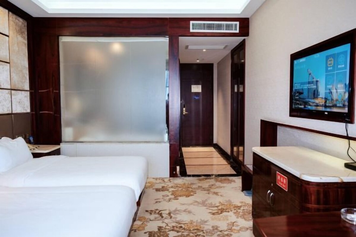 A hotel room with a bed, a desk, a television, and a shower area.