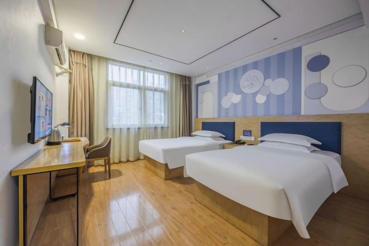 A hotel room with two beds, a desk, a chair, and a large window.