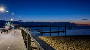 Une jetée s’avançant dans des eaux calmes au crépuscule, avec un petit bâtiment à son extrémité.