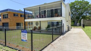 Un immeuble de deux étages doté d’un balcon, d’une enseigne indiquant qu’il propose des locations de vacances et d’une cour clôturée.