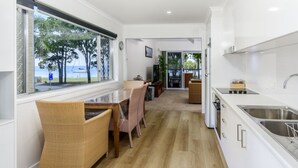 Une cuisine moderne avec un coin repas, de grandes fenêtres offrant une vue sur la mer et un chemin menant à un espace détente.