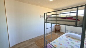 A bunk bed room with a woven mat on the floor, a chair, and a warning sign on the wall.