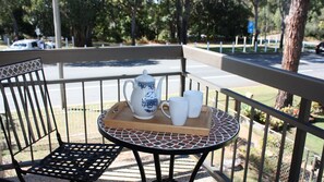 Un balcon avec une table préparée pour le thé, une chaise et une vue sur la rue.