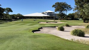 A golf course with bunkers, a clubhouse, and trees.