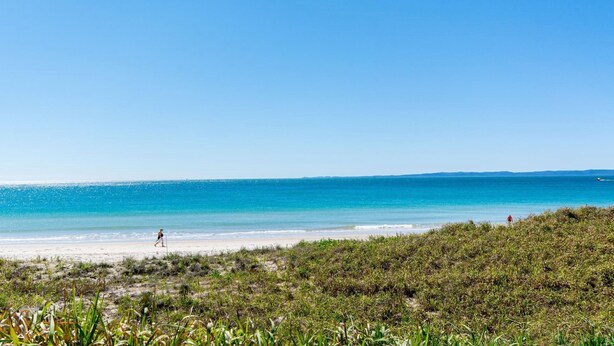 A beach with clear blue water, sandy shore, and sparse vegetation.