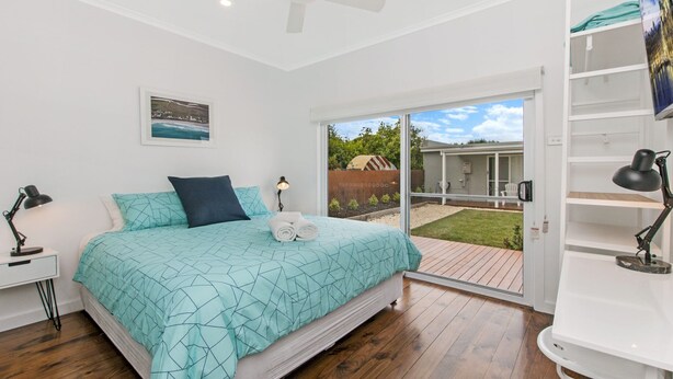 A bedroom with a bed, a nightstand, a desk, a chair, and a view of the outdoors. - Fielding's Lair - Pet Friendly (Port Fairy)