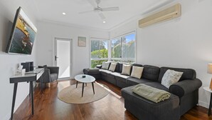 A modern living room with a sectional sofa, a round coffee table, and a TV mounted on the wall. - Fielding's Lair - Pet Friendly (Port Fairy)