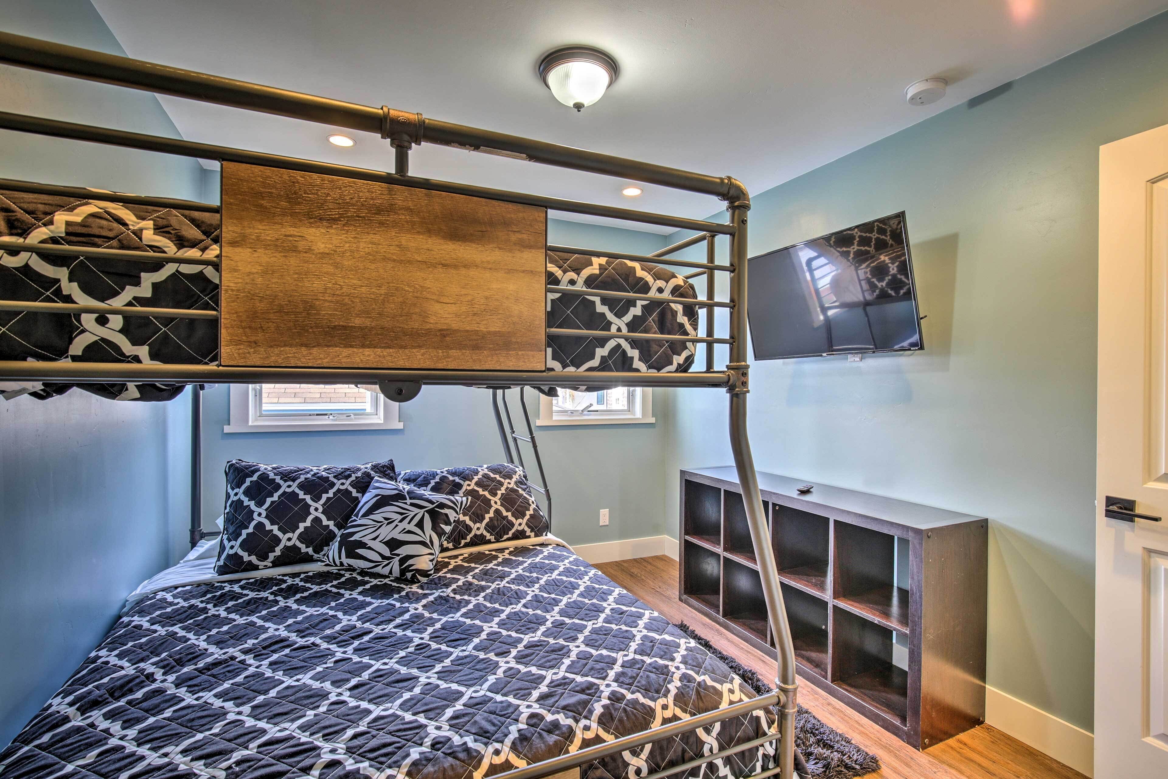 A bunk bed with a TV above it, a small shelf, and a window with blinds.