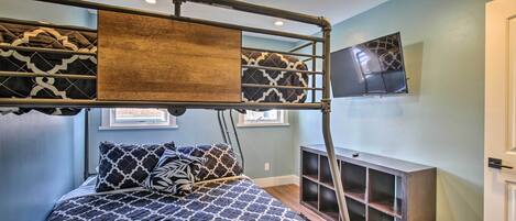 A bunk bed with a TV above it, a small shelf, and a window with blinds.