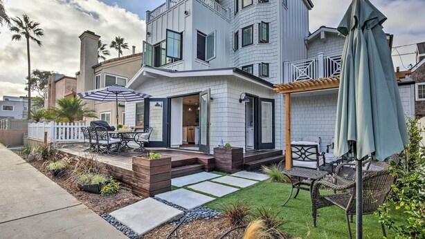 Ein modernes, zweistöckiges Haus mit Terrasse, Gartenmöbeln und einer überdachten Sitzgruppe.