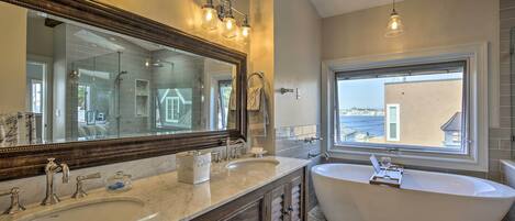 A bathroom with a large mirror, two sinks, a bathtub, and a window with a view.
