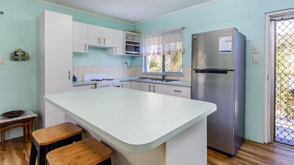 A kitchen with a large island, white cabinets, a stainless steel refrigerator, and a window with a mesh screen. - First Floor Unit Across From Water (BONGAREE)
