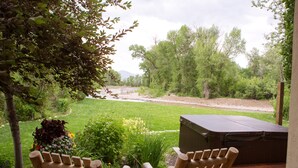 A wooden deck with two chairs, a hot tub, and a view of a river and forest. - Beautiful Driggs Townhome with Views and Hot Tub (Driggs)