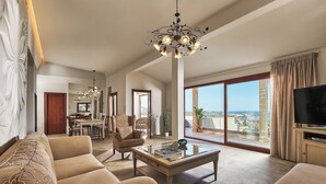 Amplia sala de estar con un sofá grande, una mesa de centro y una televisión. Hay un comedor con sillas y una mesa, y un ventanal con vistas a la ciudad.