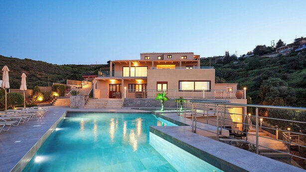 Un hotel moderno con piscina, mobiliario exterior y vistas a una colina.