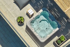 Ein Whirlpool mit Holzterrasse, ein kleiner Hocker mit Handtuch und Topfpflanzen.