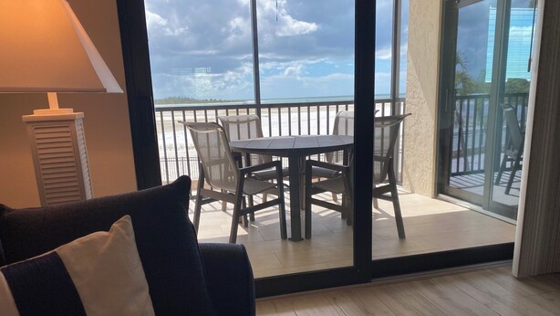 Ein Zimmer mit einer Couch, einem Tisch und Stühlen auf einem Balkon mit Blick zum Strand.