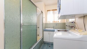 A compact kitchen with a sink, cabinets, and a window with curtains. - Walk to Suft Beach on Boyd (WOORIM)