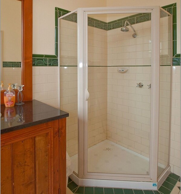 A corner shower with a glass door, a wooden cabinet with toiletries, and a green-tiled backsplash. - Situated in the CBD district with easy access to all Warrnambool has to offer (Warrnambool)