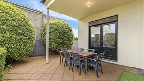 A patio with a wooden table and chairs, surrounded by neatly trimmed hedges and a brick wall. - Situated in the CBD district with easy access to all Warrnambool has to offer (Warrnambool)