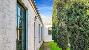 Un étroit sentier bordé d’un bâtiment blanc doté de grandes fenêtres et d’une haie bien entretenue.