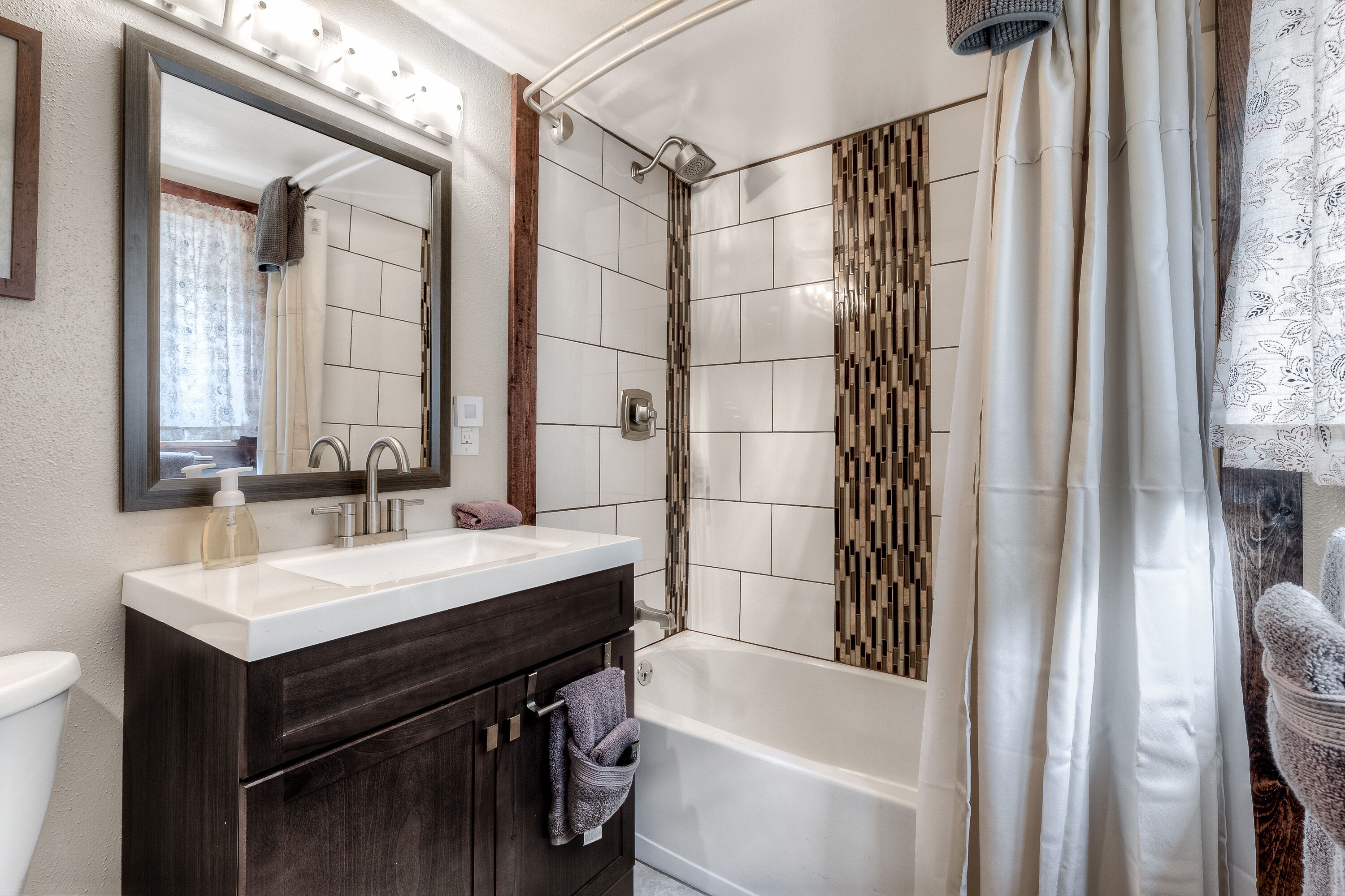 A modern bathroom with a white sink, dark vanity, and a walk-in shower with patterned tiles.