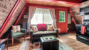 Acogedor cuarto ático con techo de madera, una puerta roja, un sofá con cojines, una mesita y un rincón de cocina.