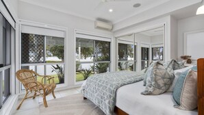 Ein Schlafzimmer mit einem großen Bett, einem Sessel und Blick ins Freie durch große Fenster.