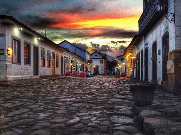 A cobblestone street lined with buildings, some with signs and lights, suggesting a historic or tourist area.