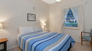 Een slaapkamer met een bed, twee bedlampen, een ingelijst schilderij aan de muur en een raam met gordijnen.