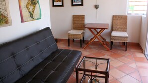 A living room with a black sofa, two wicker chairs, a small table, and artwork on the walls.