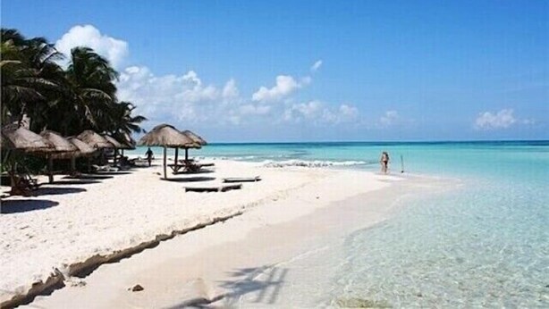 A beach with clear turquoise water, white sand, and thatched-roof structures.