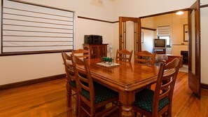 A dining room with a wooden table and chairs, a small green decorative item on the table, and a television in the background. - An inviting centrally located retreat (Warrnambool)