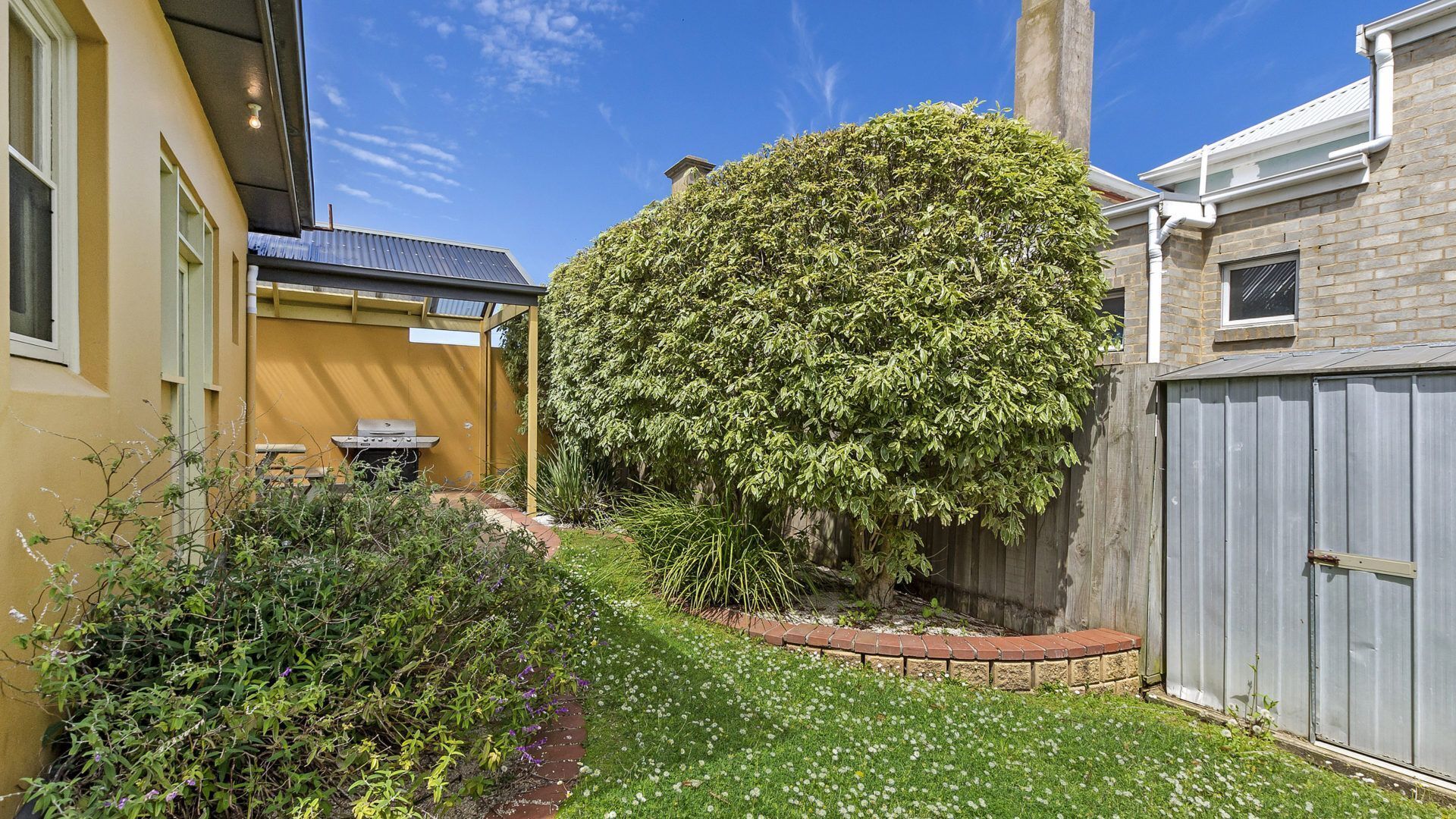 A residential garden with a well-maintained lawn, a large tree, and a barbecue area.