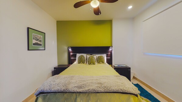 Un dormitorio con cama, mesita de noche, ventilador de techo, un cuadro en la pared y una pared de acento verde.