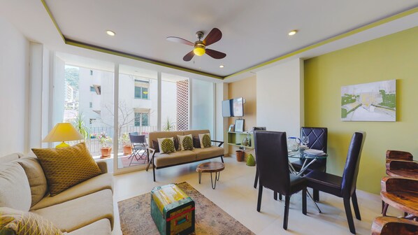 A living room with a sofa, dining table, chairs, a TV, and a ceiling fan.